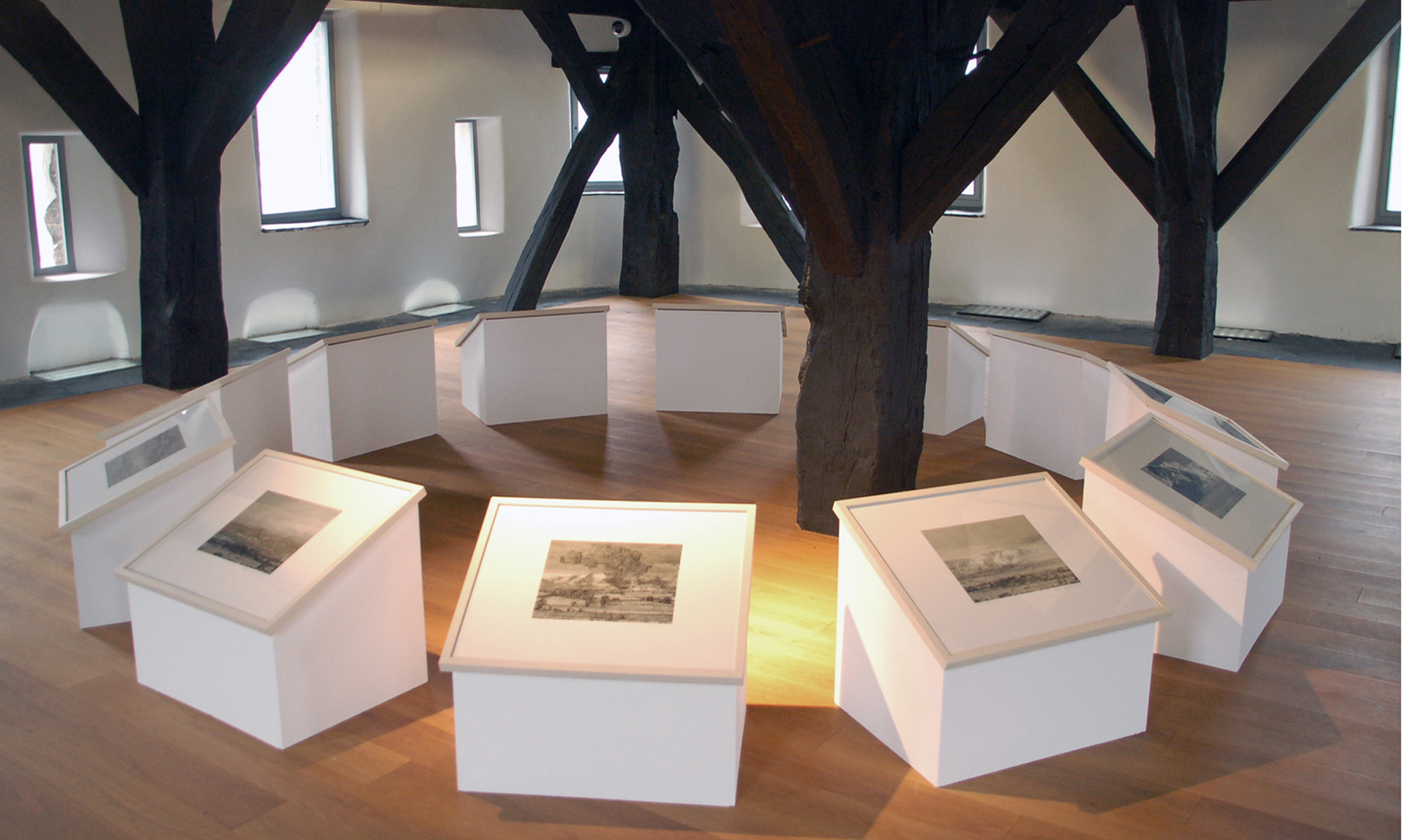 Zwölf weiße Holzobjekte mit schwarzweißen Grafiken auf einem Holzfußboden im Kreis. Sie befinden sich im Turmzimmer des Museums Boppard.